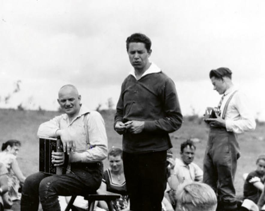 Hermann Huffziger mit Akkordeon = Ziehharmonika auf einem Hocker sitzend, neben dem Tanzlehrer und Volkstanzforscher Ludwig Burkhardt.